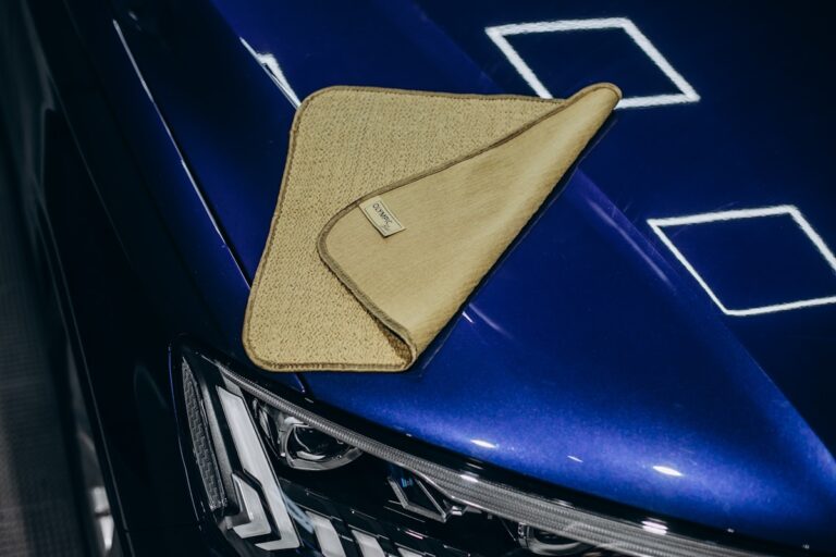 Close-up of tan waffle-weave microfiber cloth resting on freshly detailed blue car hood, ceramic coating shine