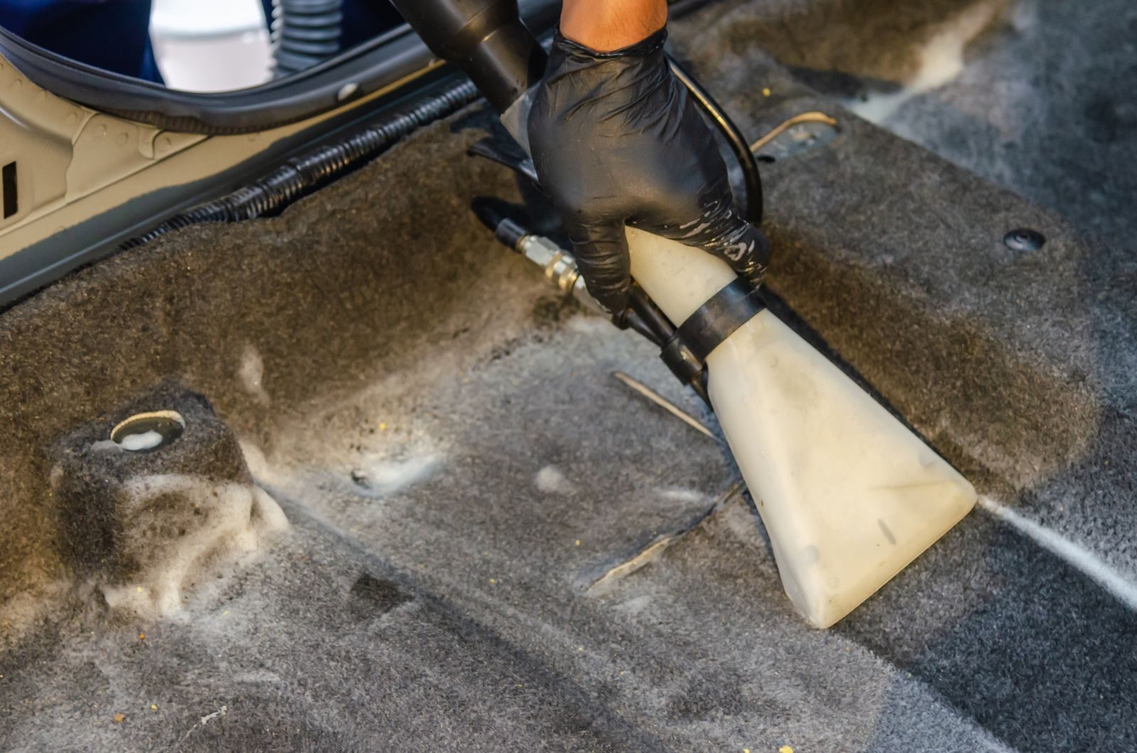 Extractor wand pulling shampoo and dirt out of car carpet during an interior detail