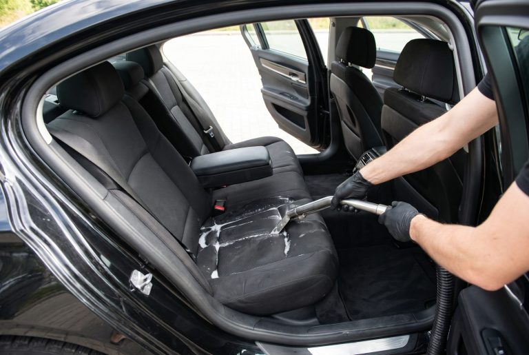 Deep cleaning a cloth car seat with an extractor, detailer wearing black latex gloves